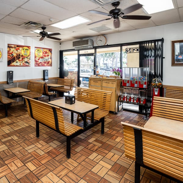 Interior of Fiesta Pizza with wooden benches, tables, pizza posters, and gumball machines.