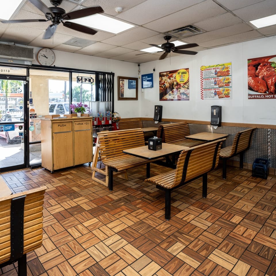 Interior of Fiesta Pizza with wooden benches, tables, and pizza deal posters on the walls.