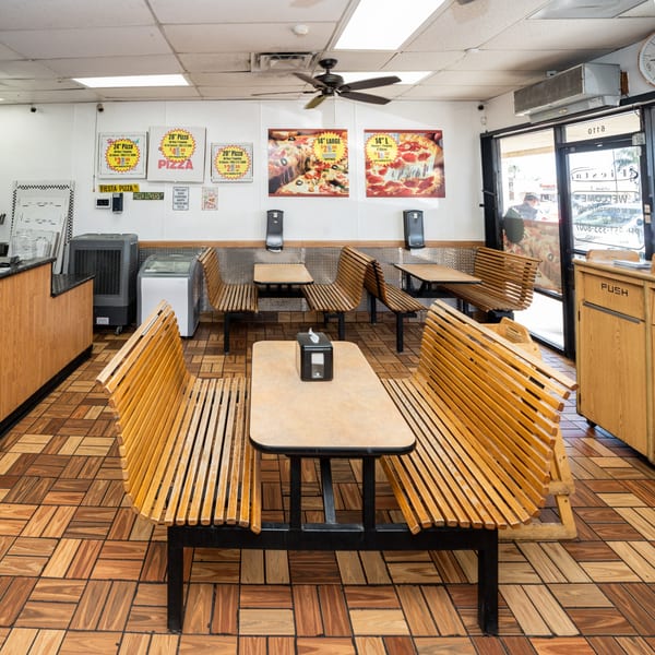 Interior of Fiesta Pizza with wooden benches, tables, and pizza advertisements on the wall.